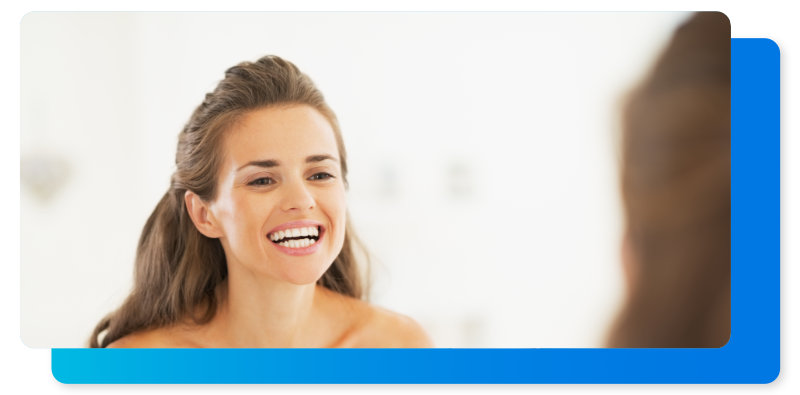 Una mujer con los protectores invisibles de Sonrisas Club sonriendo en un espejo.