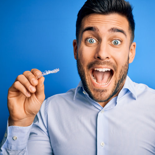 Hombre sonriente que sostiene los alineadores transparentes Smiles Club y muestra una gran dentadura.